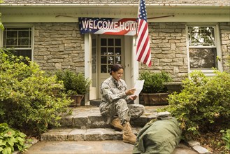 Smiling African American soldier sitting on front stoop reading letter