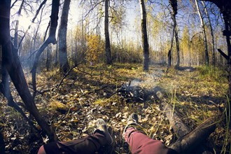 Fish-eye lens view of legs sitting by smoking campfire