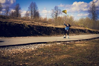 Caucasian girl on inline skates flying kite on rural road
