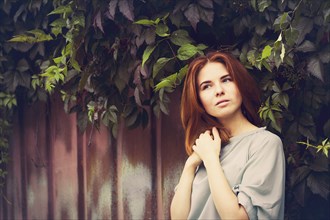 Caucasian woman standing under leaves by fence