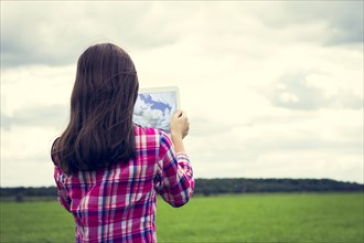 Caucasian girl taking photograph with tablet computer in grassy field
