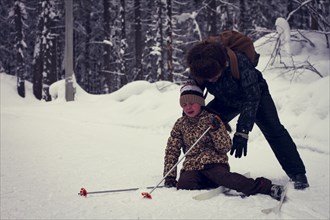 Caucasian father helping cross-country skiing daughter falling in snow
