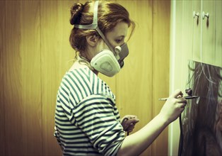 Artist in gas mask airbrushing painting in studio