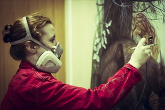 Artist in gas mask airbrushing painting in studio