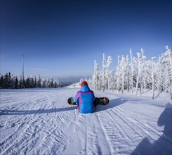 Caucasian snowboarder sitting on snowy slope