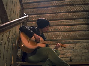 Caucasian man playing guitar on staircase