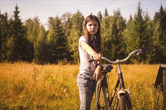 Caucasian teenage girl pushing bicycle in field
