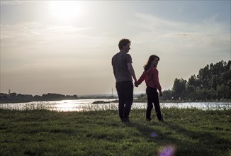 Caucasian brother and sister holding hands near river at sunset