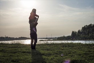 Caucasian brother carrying sister on shoulders near river at sunset