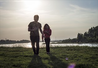 Caucasian brother and sister walking near river at sunset