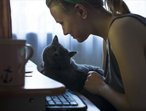 Caucasian woman petting cat at computer