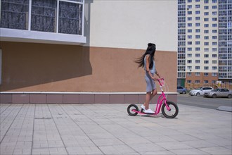 Caucasian woman riding push scooter on city sidewalk