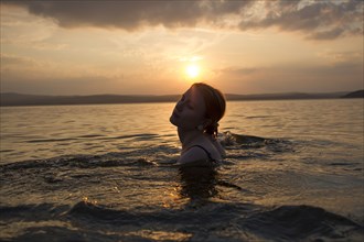 Caucasian woman swimming in lake at sunset