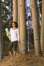 Mixed race woman holding yoga mat in forest
