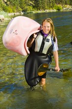 Caucasian teenager carrying kayak in river