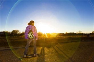 Chinese girl skateboarding on road at sunset