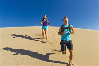 Hispanic couple running on sand dune
