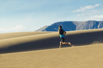 Hispanic man running on sand dune
