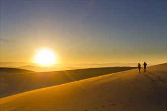Hispanic couple walking on sand dune at sunset