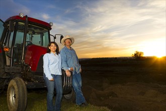 Hispanic couple standing near tractor on farm