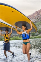 Hispanic couples carrying paddle boards in water