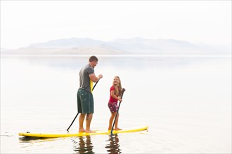 Caucasian father and daughter riding paddle board
