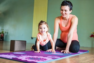 Mixed Race expectant mother and daughter on exercise mat
