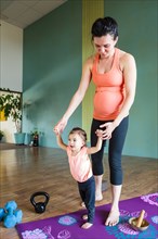 Mixed Race expectant mother holding hands of daughter on exercise mat