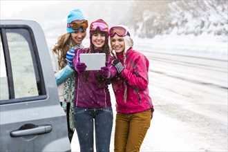 Women posing for selfie with digital tablet near car in winter