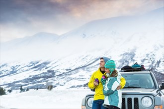 Caucasian couple hugging and leaning on car in winter