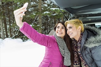Women at car posing for cell phone selfie in winter