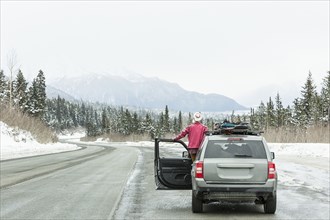 Caucasian woman standing in car in winter admiring scenic view