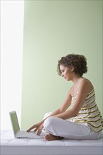 Mixed race woman sitting on sofa using laptop