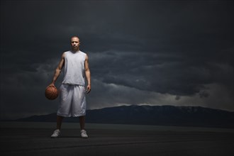 Mixed race basketball player standing with storm clouds in distance