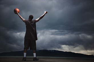 Mixed race basketball player standing with storm clouds in distance