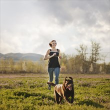 Caucasian woman running in field with dog