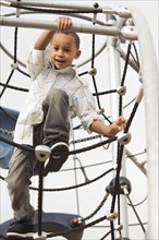 Mixed race boy climbing on structure in playground