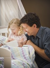 Caucasian father reading book to daughter in bed