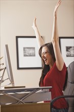 Caucasian woman cheering at desk in home office