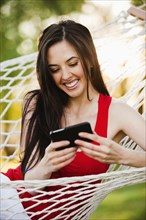 Caucasian woman in hammock text messaging on cell phone