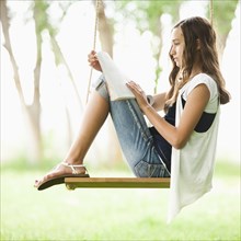 Caucasian girl reading book on swing