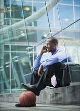 Black businessman sitting outdoors with basketball talking on cell phone