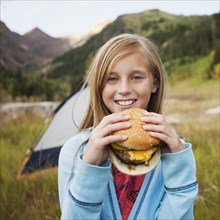 Caucasian girl eating cheeseburger at campsite
