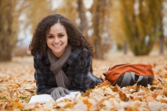 Caucasian woman laying in autumn leaves reading book