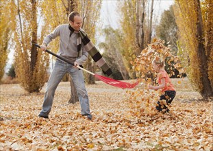 Caucasian father and daughter raking autumn leaves