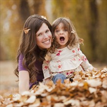 Caucasian mother and daughter playing in autumn leaves
