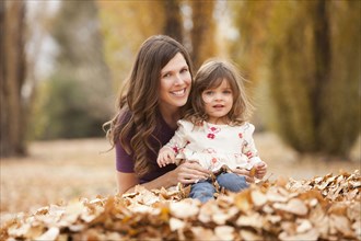 Caucasian mother and daughter playing in autumn leaves