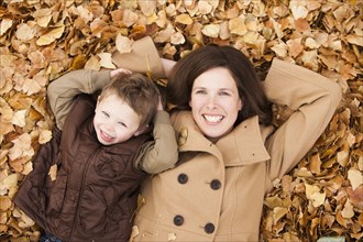 Caucasian mother and son laying autumn leaves