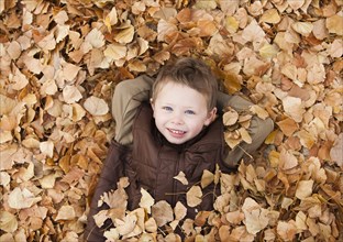Caucasian boy laying in autumn leaves