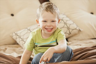 Smiling Caucasian boy sitting on bed